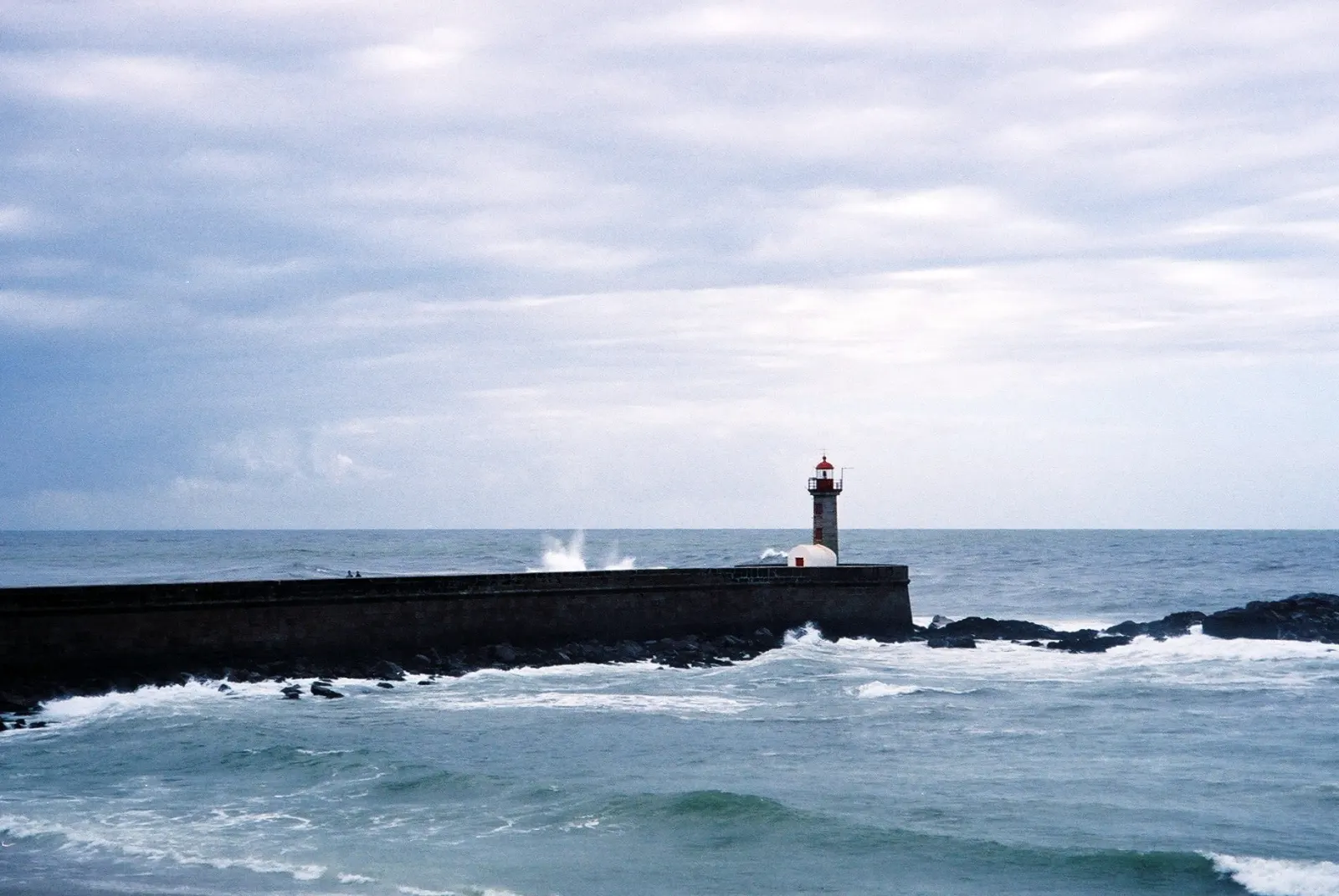The Felgueiras lighthouse at the end of its stone pier at Foz do Douro, Atlantic waves breaking against it